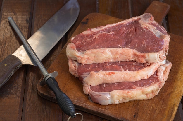 Steaks argentins crus sur une planche à découper en bois avec couteau et acier à aiguiser