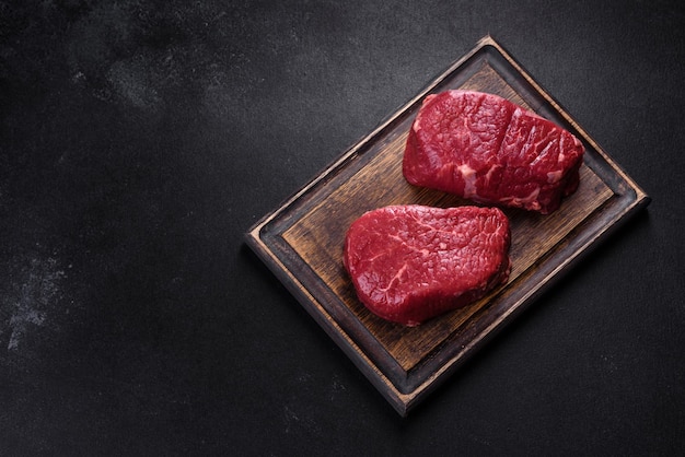 Steaks de boeuf cru sur une planche à découper avec des épices sur un fond de pierre