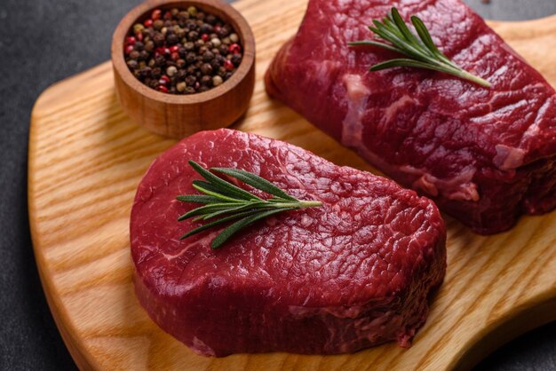 Steaks de boeuf cru sur une planche à découper avec des épices sur un fond de pierre