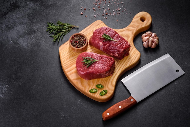 Steaks de boeuf cru sur une planche à découper avec des épices sur un fond de pierre