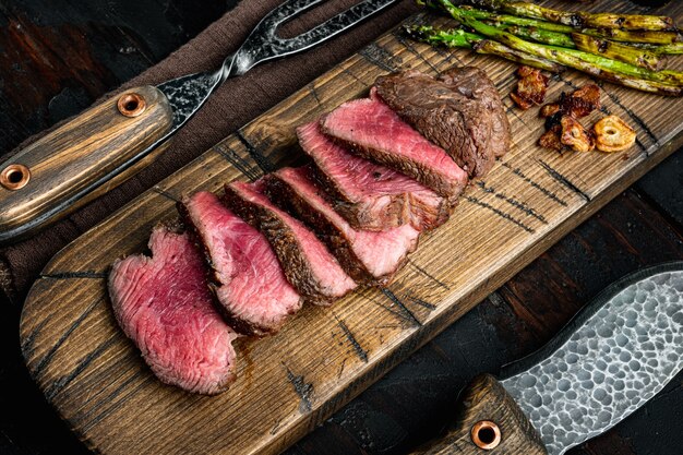 Steaks de boeuf grillés avec couteau à viande et fourchette, sur la vieille table en bois sombre