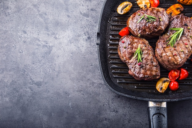 Steaks de boeuf grillés dans une poêle grillée avec champignons tomates et romarin.