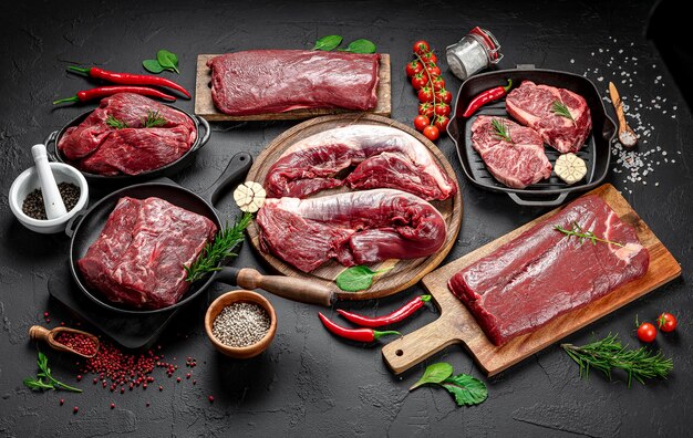 Photo steaks de bœuf marbrés biologiques crus avec des épices sur une planche à découper en bois sur une pierre d'ardoise noire ou un fond en béton vue supérieure avec espace de copie