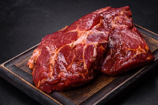 Steaks de bœuf marbrés crus avec des épices sur une planche à couper en bois