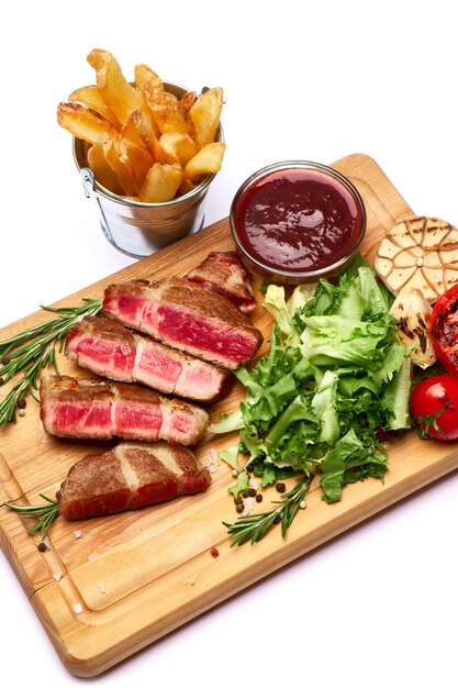 Steaks de boeuf rôtis en tranches grillés pomme de terre et sauce sur planche à découper en bois