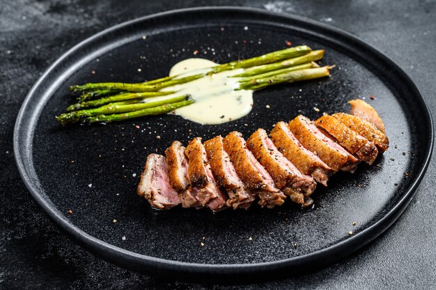 Steaks de canard grillés aux asperges. Fond noir.