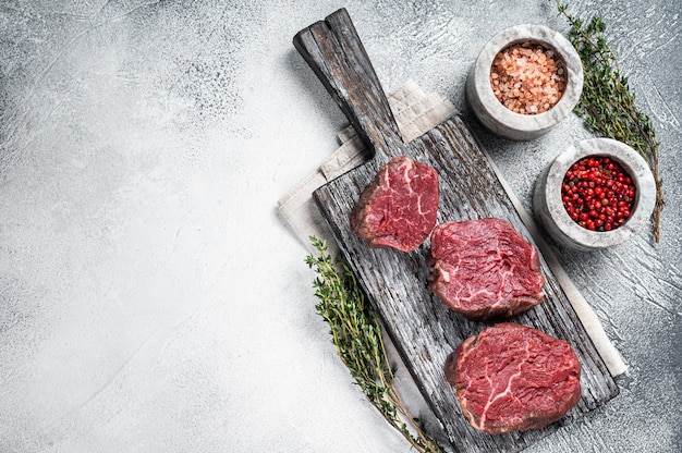 Steaks crus de boeuf de filet mignon sur une planche en bois avec du sel et du poivre. Fond blanc. Vue de dessus. Espace de copie.