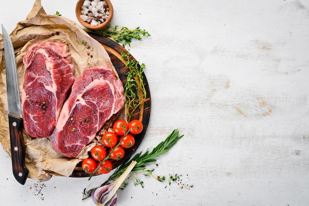 Steaks de faux-filet juteux crus aux épices sur une table en bois blanche Vue de dessus Espace libre pour votre texte