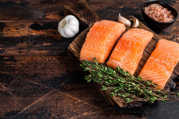 Steaks de filet de poisson saumon cru frais sur planche de bois au thym. Fond en bois sombre. Vue de dessus. Espace de copie.