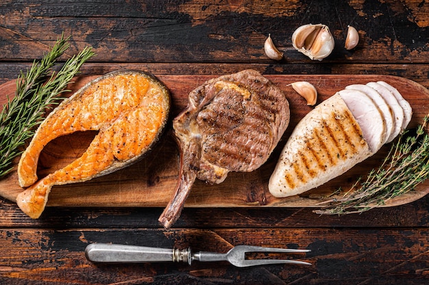 Steaks grillés au barbecue - saumon, faux-filet de boeuf et filet de poitrine de dinde sur une planche de bois. Fond en bois. Vue de dessus.