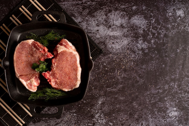 Steaks juteux crus avec des assaisonnements dans une poêle noire prête à rôtir sur fond de béton rustique.