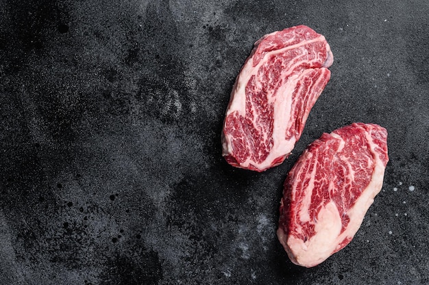 Steaks de mandrin crus, viande de bœuf de qualité supérieure sur une planche de boucher. Fond noir. Vue de dessus. Espace de copie.