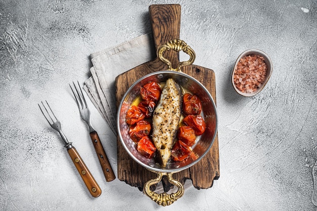 Steaks de poisson de flétan frit à la tomate dans une poêle. Fond blanc. Vue de dessus.