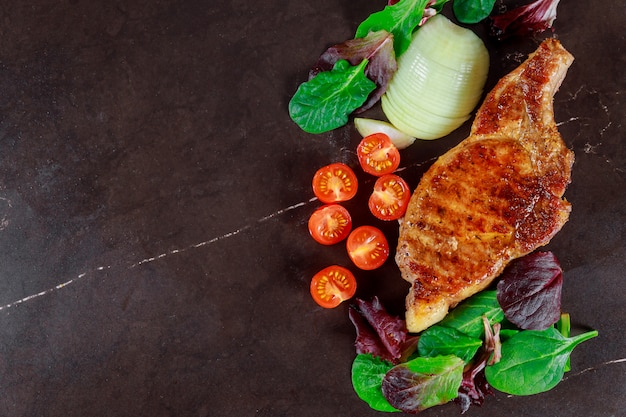 Steaks de porc aux légumes grillés et assaisonnement sur fond sombre