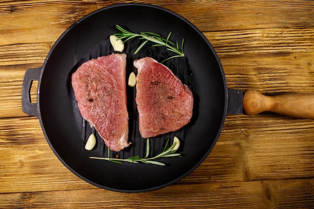 Steaks de porc crus prêts à être préparés avec de l'ail au romarin et des épices dans une poêle à frire en fonte sur une table en bois Vue de dessus