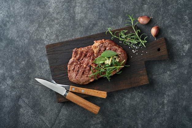 Steaks Tranches de steak de viande grillée New York ou Ribeye avec épices romarin et poivre sur planche de marbre noir sur fond de bois ancien Vue de dessus Maquette