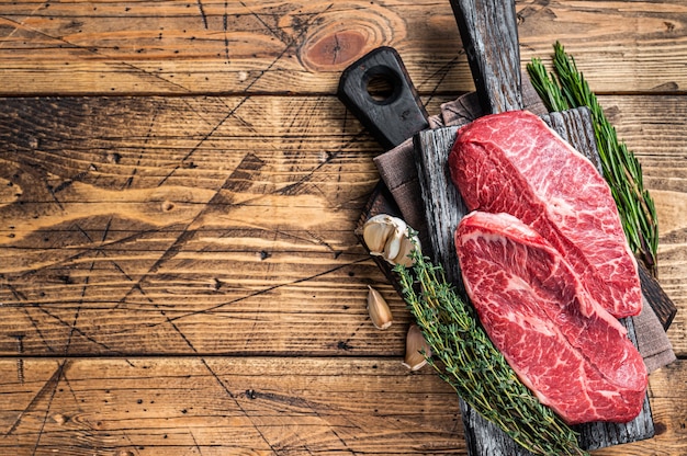 Steaks de viande de boeuf à lame supérieure d'épaule crue sur une planche de boucher en bois avec des herbes