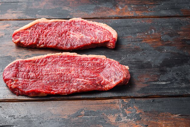 Steaks de viande de bœuf picanha bio, sur fond de bois ancien foncé, espace de vue latérale pour le texte.