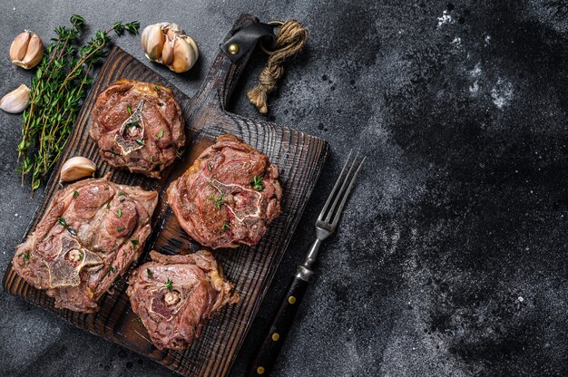 Steaks de viande de cou d'agneau grillés sur une planche de bois aux herbes. Fond noir. Vue de dessus. Espace de copie.