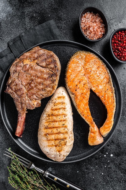 Steaks de viande grillés - saumon de poisson, veau de boeuf et filet de dinde. Fond noir. Vue de dessus.