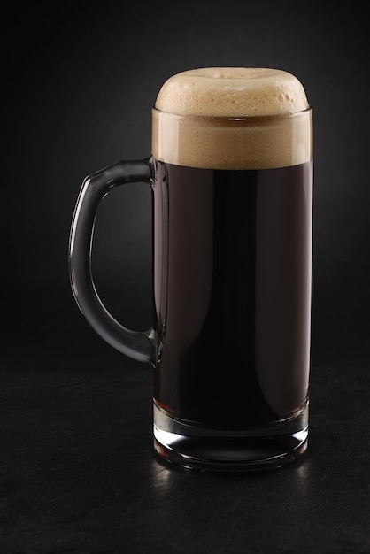 Stein avec bière stout fraîche avec bouchon de mousse sur fond noir