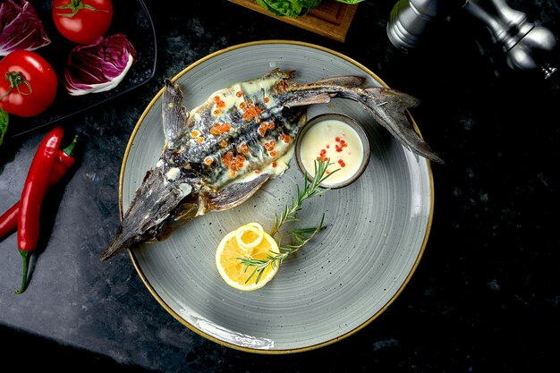 Sterlet cuit au four avec sauce blanche et caviar rouge, servi dans une assiette grise sur une table en marbre foncé. Nourriture de restaurant. Fruits de mer