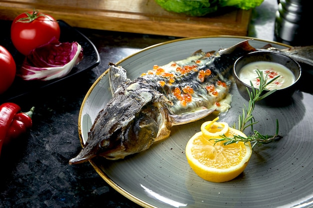 Sterlet cuit au four avec sauce blanche et caviar rouge, servi dans une assiette grise sur une table en marbre foncé. Nourriture de restaurant. Fruits de mer