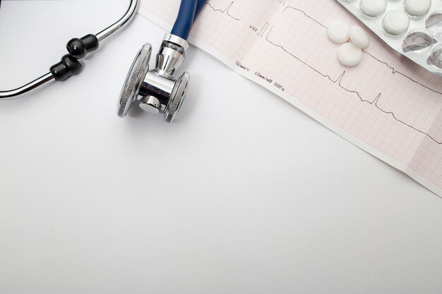 Stéthoscope bleu cardiogramme et pilules se trouvent sur une table blanche Vue de dessus