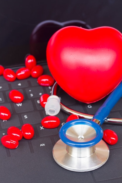 Stéthoscope bleu avec des pilules rouges sur un clavier d'ordinateur portable noir