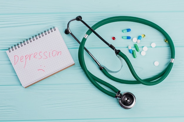 Stéthoscope avec capsules sur fond bleu. Dépression écrite sur le bloc-notes.