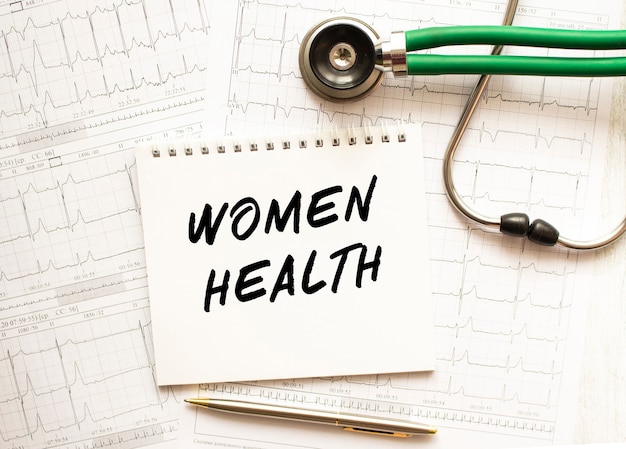 Stéthoscope avec cardiogramme et bloc-notes avec texte WOMEN HEALTH.