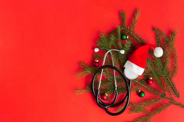 Stéthoscope médical avec chapeau de père Noël et arbre de Noël sur fond rouge