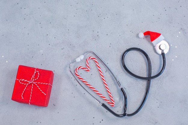 Stéthoscope médical dans un chapeau de père noël rouge avec boîte-cadeau et bonbons