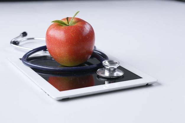 Stéthoscope médical et pomme rouge allongé sur une tablette isolée sur fond blanc
