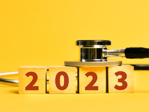 Stéthoscope avec numéro 2023 sur cubes en bois sur fond jaune.