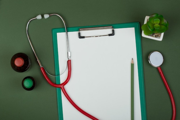 Stéthoscope rouge sur le lieu de travail du médecin et presse-papiers vide sur fond de papier vert