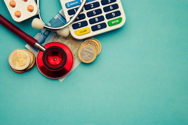 Stéthoscope rouge sur un tas de pièces de monnaie, pilules sur bleu. fond Médecine et soins de santé.