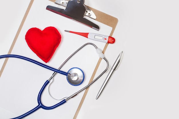 Un stéthoscope et un thermomètre sur un presse-papiers avec un coeur rouge en tissu