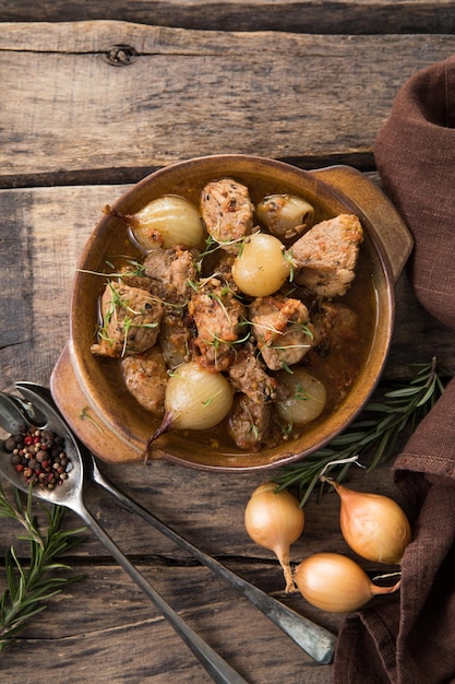 Stifado - délicieux ragoût de boeuf méditerranéen avec bulbes d'oignons, cannelle et épices dans une casserole, sur une table en bois noir, vue d'en haut, gros plan