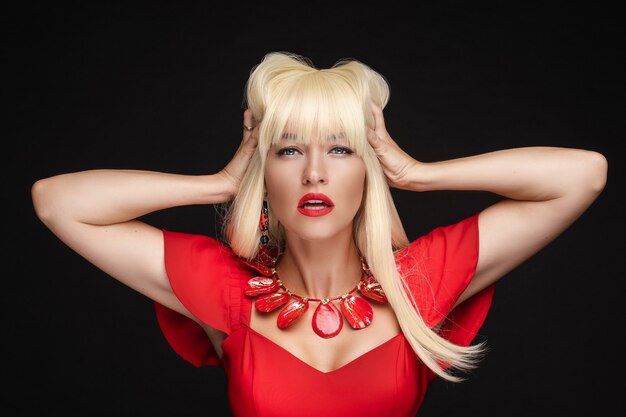 Stock photo de femme blonde sexy avec des lèvres rouges en robe rouge et accessoires rouges tenant les bras dans ses cheveux. Elle ouvre légèrement la bouche.