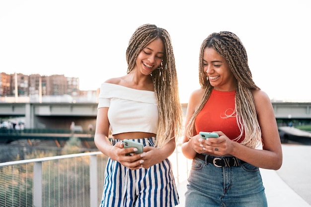 Stock photo de jeunes sœurs afro-américaines riant et utilisant leurs téléphones dans la rue