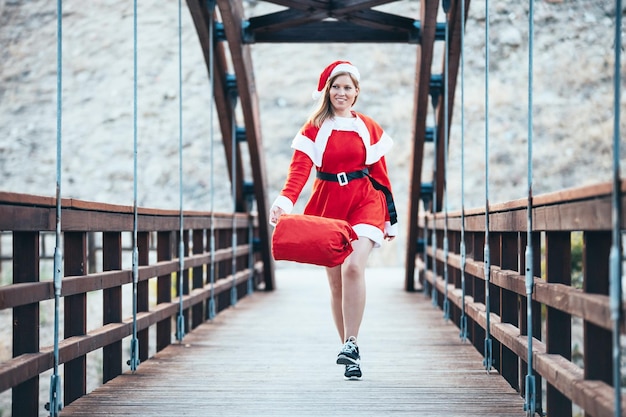 Stock photo de Mama Noel jouant joyeusement avec le sac rouge de cadeaux sur un pont en bois le temps de Noël