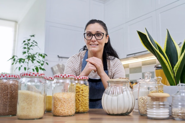 Stocker de la nourriture dans la cuisine femme avec des bocaux et des récipients parler et regarder la caméra