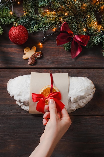 Photo stollen de noël avec du marzipan et des fruits secs sur fond sombre lumière de noël festive humeur de vacances joyeuse temps de mains féminines décorent le stollen pour le marché