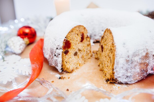 Stollen de Noël rond traditionnel fait de fruits secs et de noix saupoudrés de sucre en poudre sur fond de décor de Noël avec des bougies. Petit gâteau de Noël traditionnel.