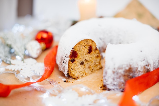 Stollen de Noël rond traditionnel fait de fruits secs et de noix saupoudrés de sucre en poudre sur fond de décor de Noël avec des bougies. Petit gâteau de Noël traditionnel.