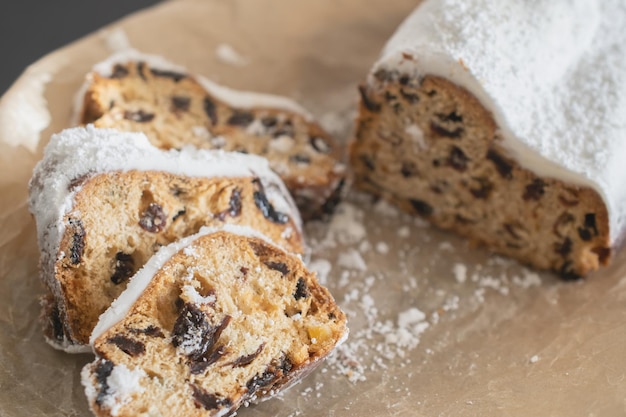 Stollen de Noël traditionnel fait de fruits secs et de noix saupoudrés de sucre en poudre sur fond de décor de Noël avec des bougies. Petit gâteau de Noël traditionnel.