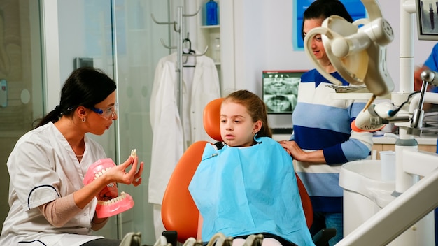 Stomatologue expliquant à l'enfant la chirurgie à l'aide d'un modèle en plâtre de la mandibule en extrayant une dent. Dentiste pédiatrique tenant une maquette de squelette de dents, échantillon de mâchoire humaine parlant.