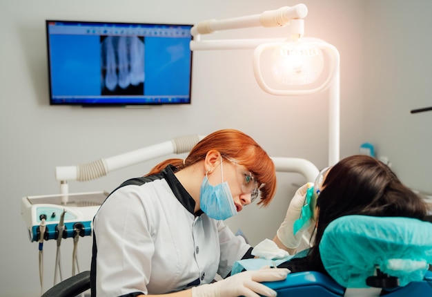 Stomatologue féminin dans des gants de protection et un masque examinant les dents du patient Traitement des caries dentiste au bureau de la clinique dentaire Personnes médecine stomatologie et concept de soins de santé