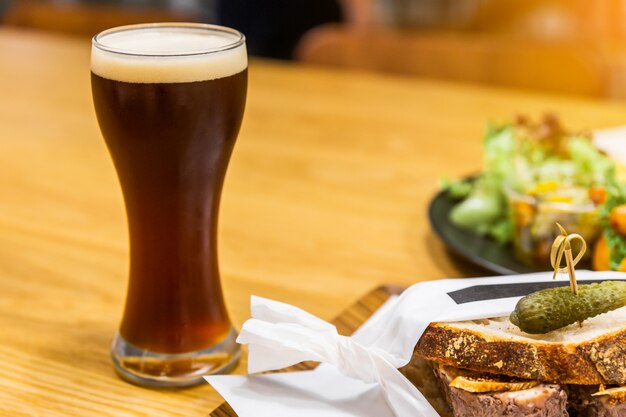 Stout (bière noire) avec de la mousse dans un verre à boire sur une table en bois avec des aliments flous